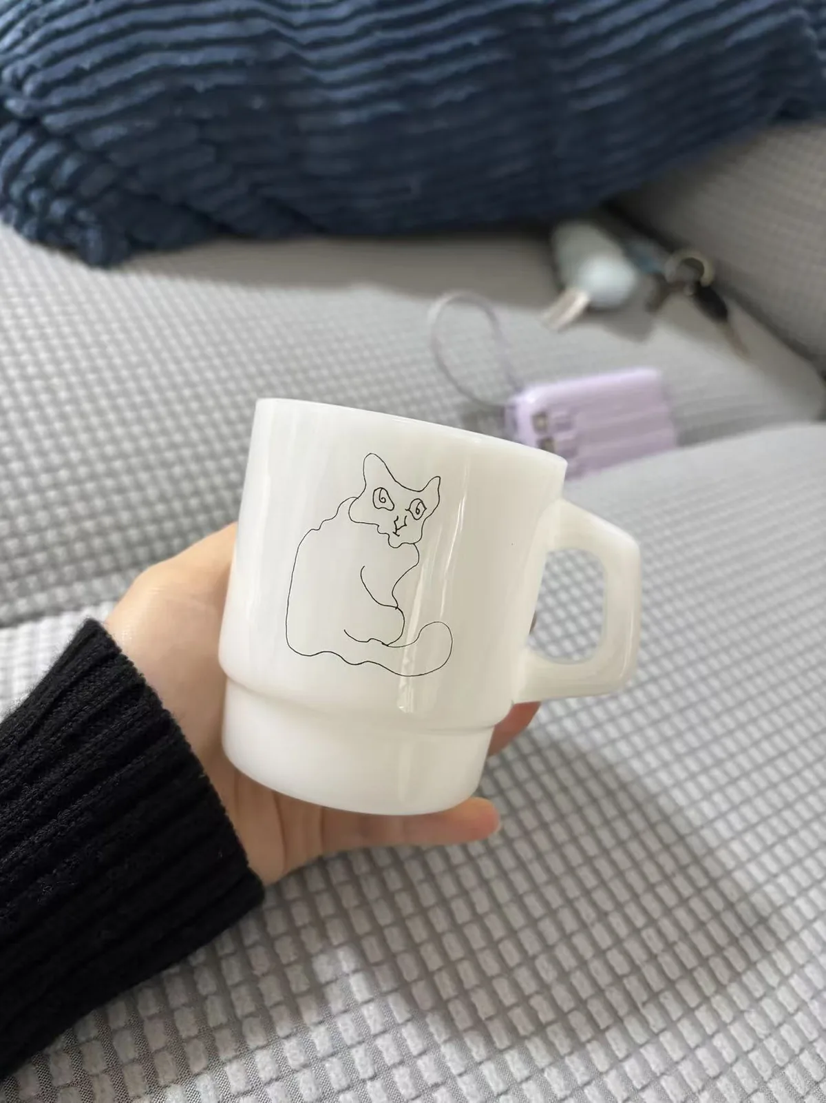 手中托着一只白色奶玉杯,杯身印有回头注视的猫线稿