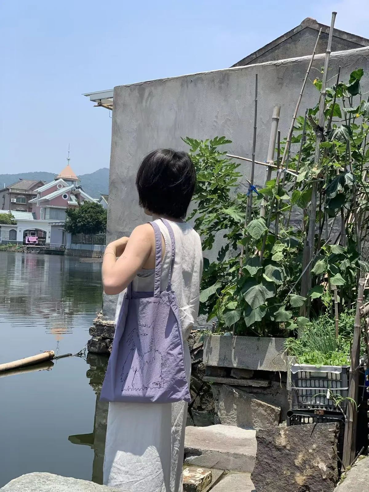 一位女性背着淡紫色猫线稿布包站在水边