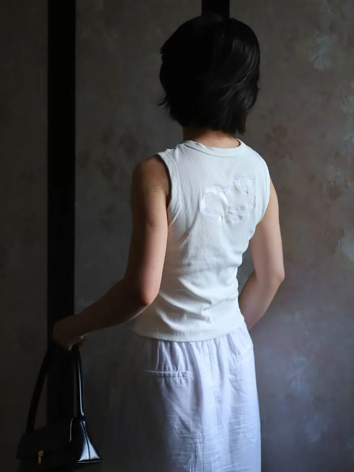 一位女性穿着背后带浅色猫形刺绣的白色背心